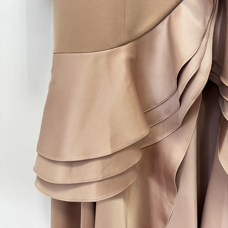 Close-up of a taupe-beige dress with a structured bodice and layered draped satin ruffle skirt details.