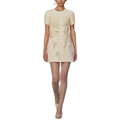 A model wearing a short-sleeve cream-colored mini dress with gold floral embroidery, shown against a plain white background.