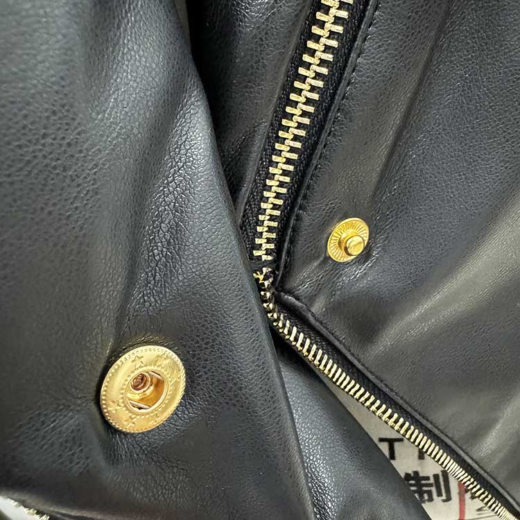 Close-up of a black fitted leather jacket with zippers showcasing detailed stitching and gold accents