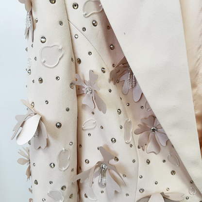 Close-up of a cream-colored textured jacket featuring 3D floral appliqués and silver rhinestone embellishments, with a matching cream satin lapel.