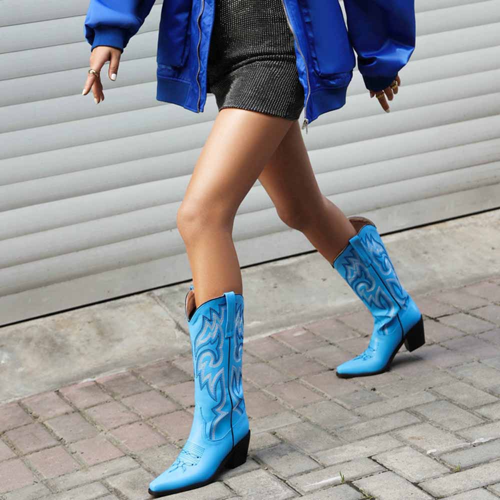Fashionable woman wearing colorful embroidered cowgirl boots with a stylish blue jacket and grey dress