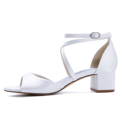 Elegant criss cross satin block heel sandals in white with an ankle strap for stylish occasions.