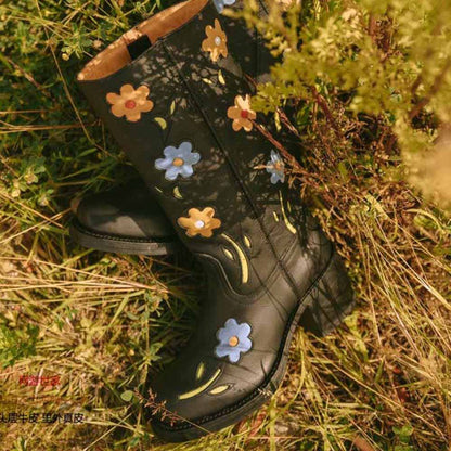 Floral embroidered boots in black with colorful flower designs against a natural backdrop