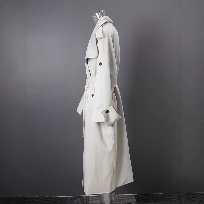 Side view of an oversize women's trench coat in cream color with a belted waist and classic design