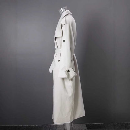 Side view of an oversize women's trench coat in cream color with a belted waist and classic design