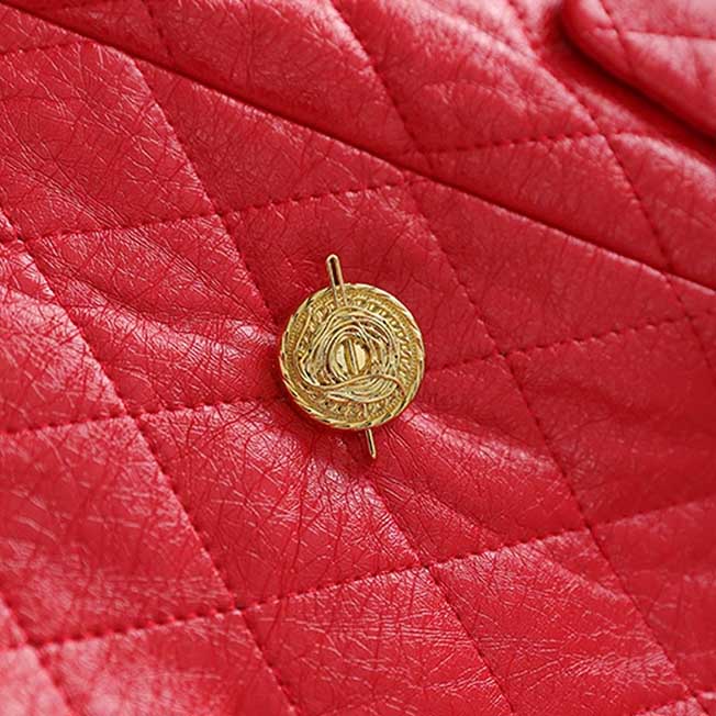 Detailed view of a gold button on a red faux leather mini dress with quilted texture