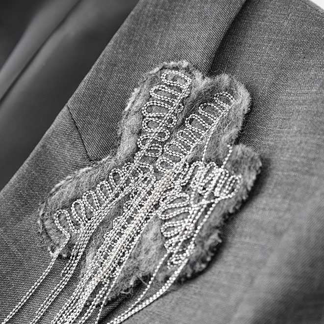 Women's grey tailored pantsuit featuring a stylish embellishment on the blazer