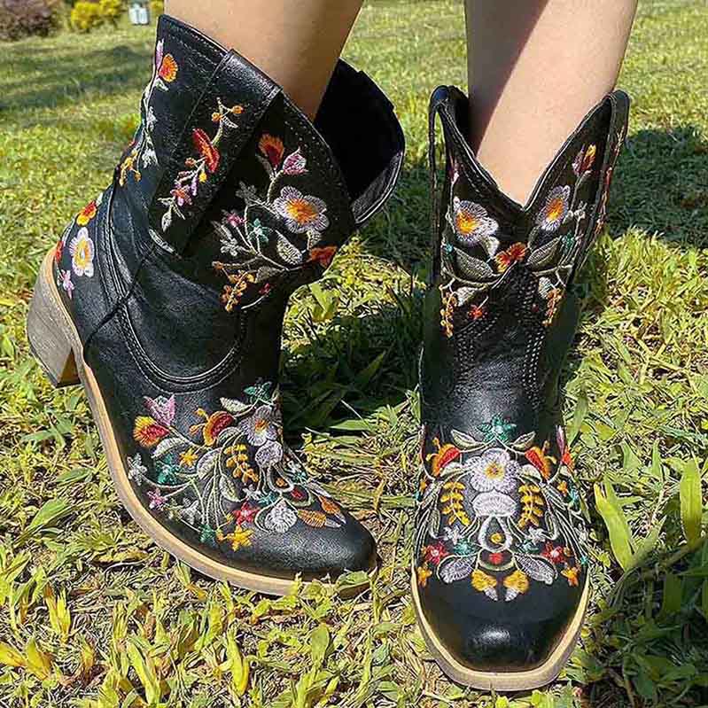Vintage flower embroidered cowgirl boots in black with colorful floral designs on a grassy background