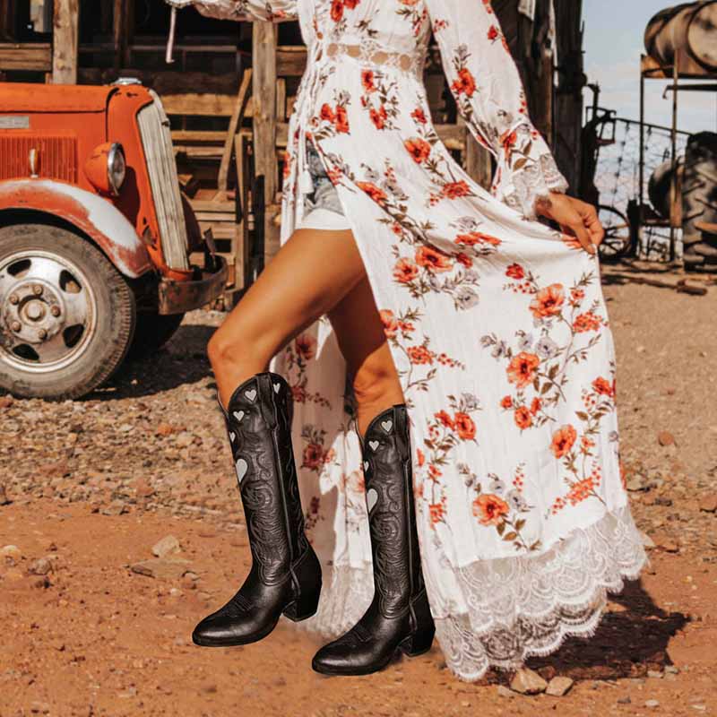 Stylish women's embroidery heart cowgirl boots paired with a floral dress in a rustic outdoor setting